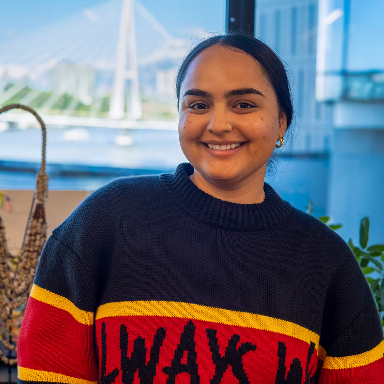 Ta’Kura Madsen, proud Kuku Yalanji woman and CareerTrackers 2022 graduate, smiling in an office with a river and bridge behind her.
