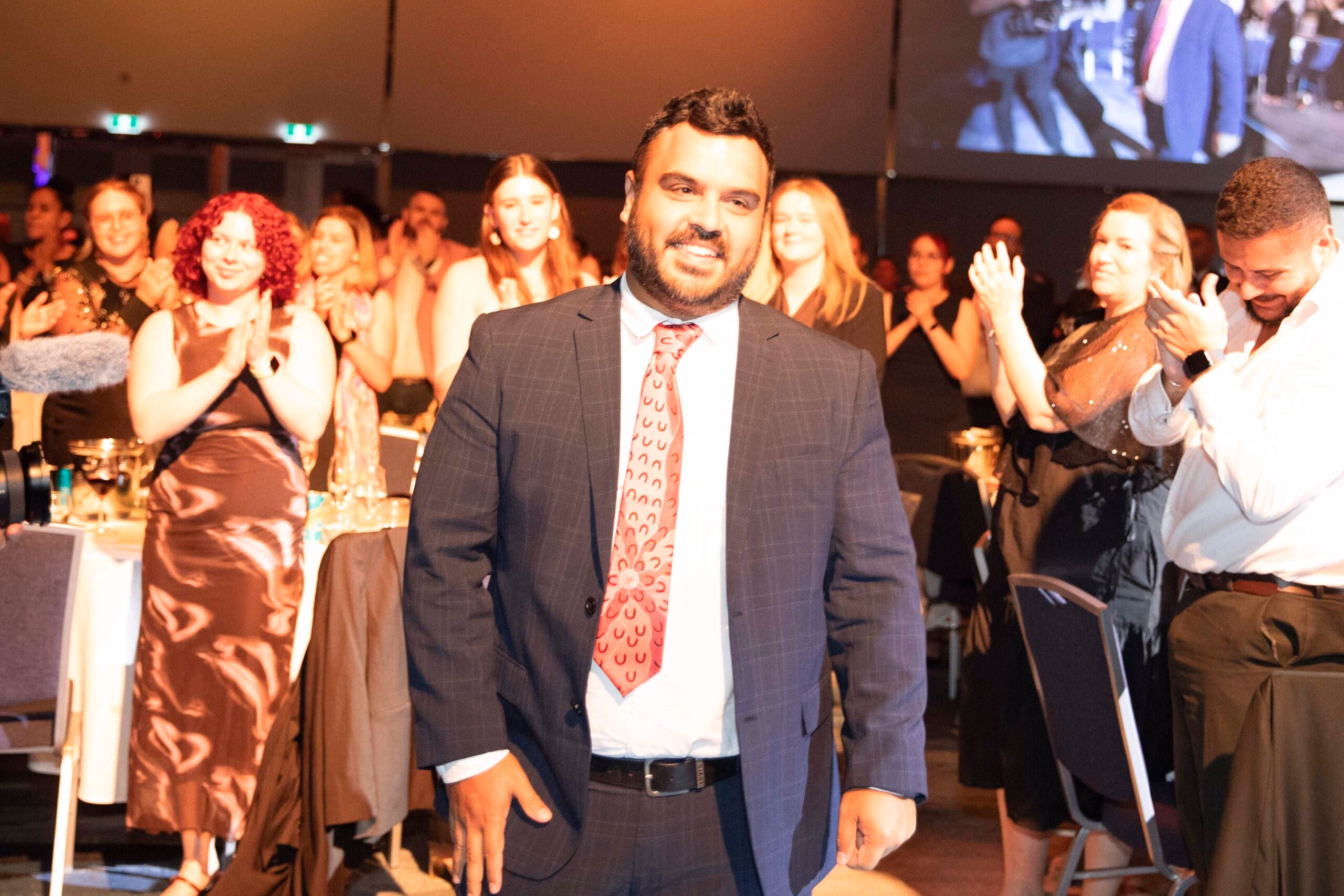 A CareerTrackers graduate walking through a room of applauding guests.